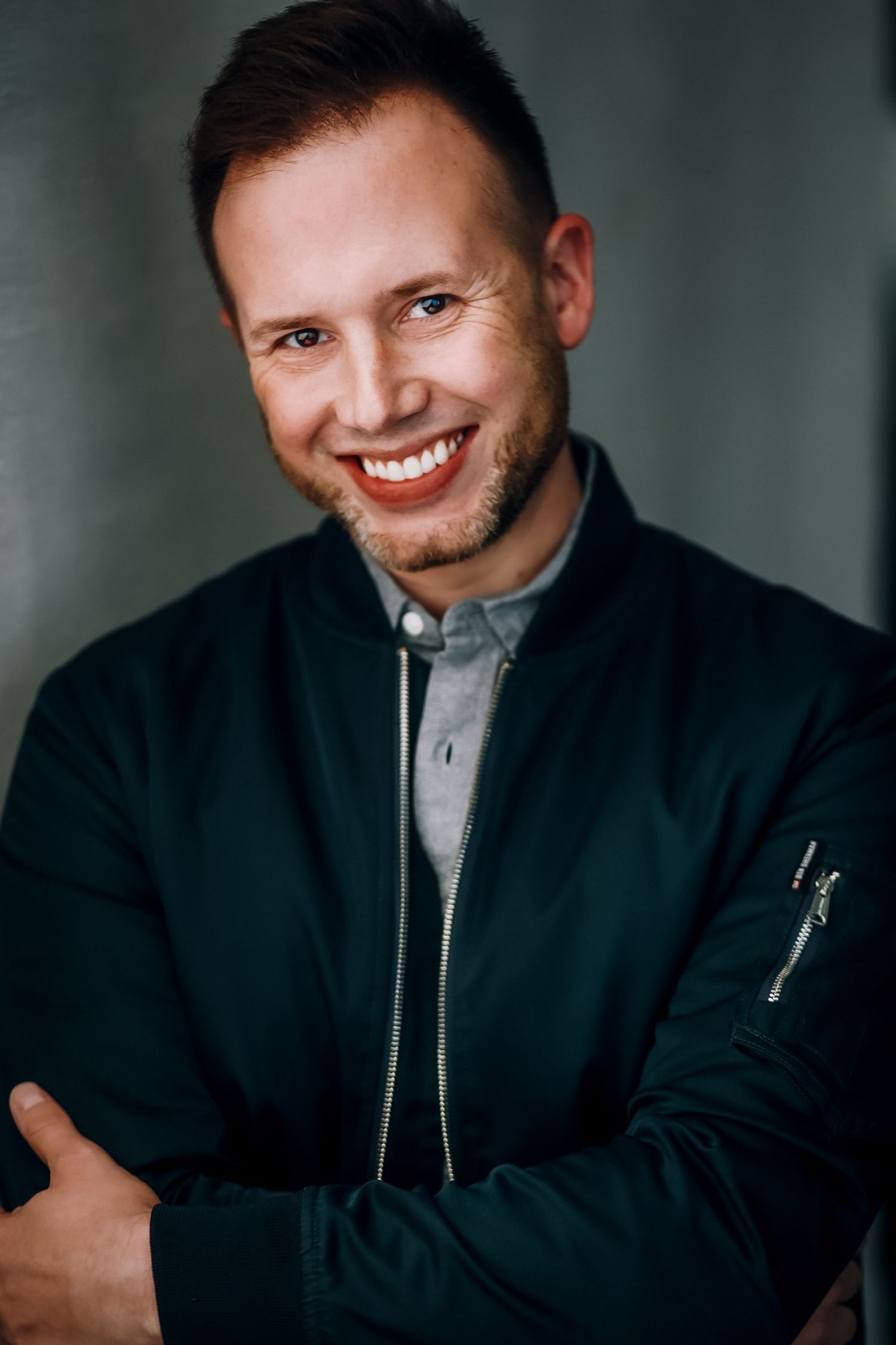 Casual outdoor portrait of someone in plaid and denim jacket with short styled hair.