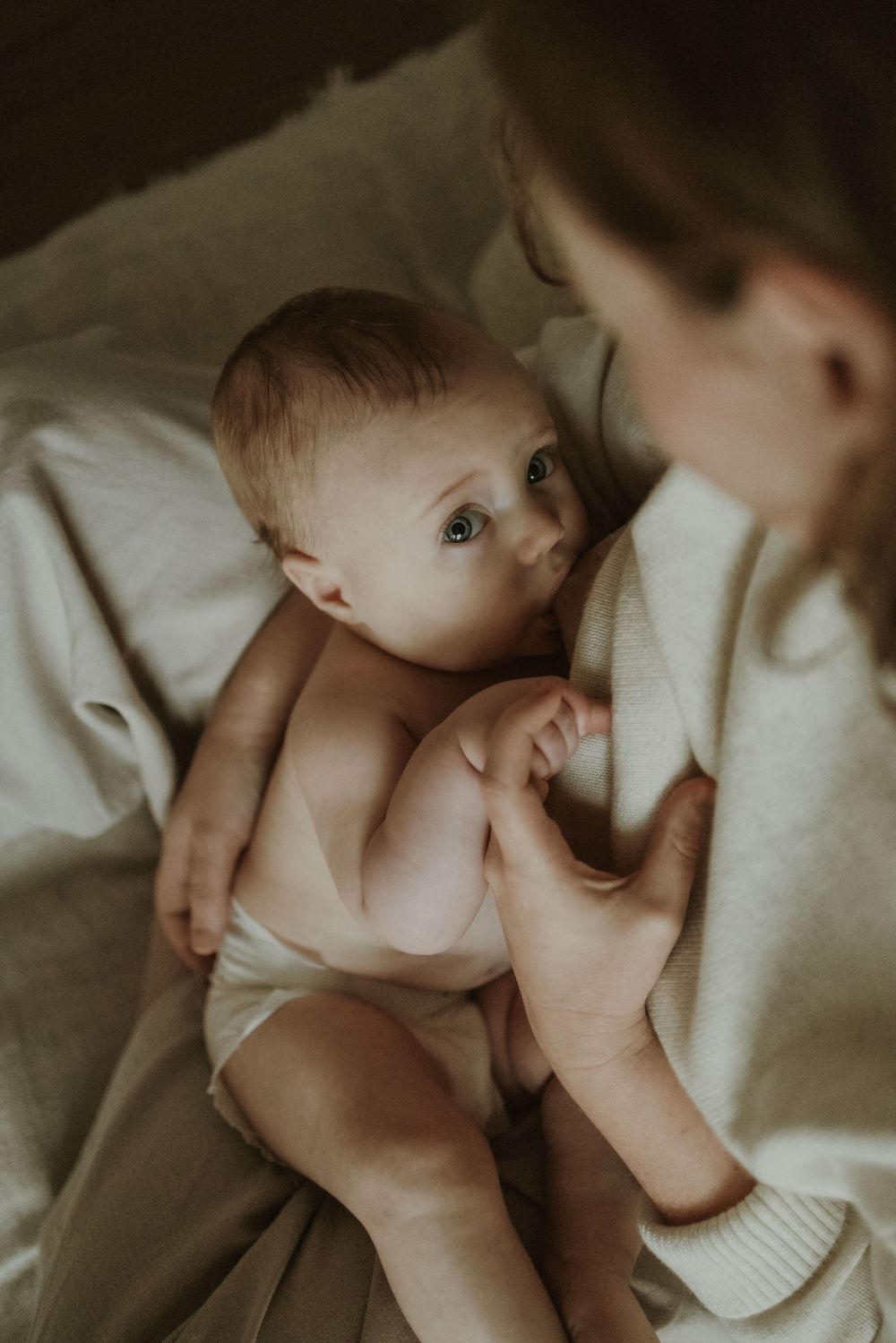 A tender moment between parent and baby lying on white bedding in soft natural light.