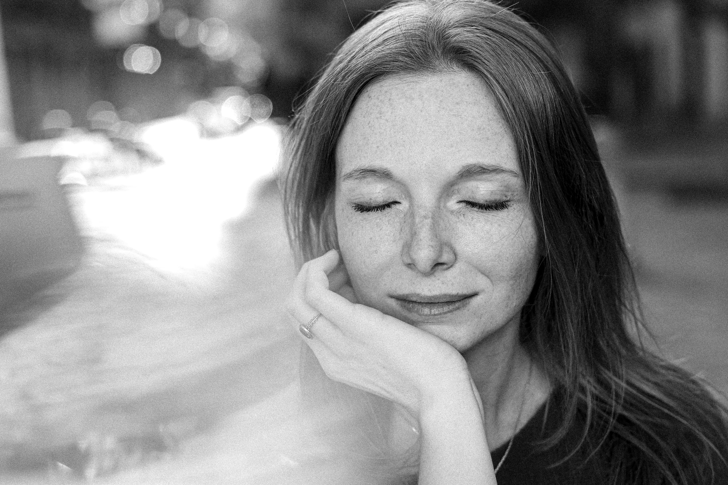 A black and white portrait of a freckled woman with closed eyes resting her chin on her hand peacefully.