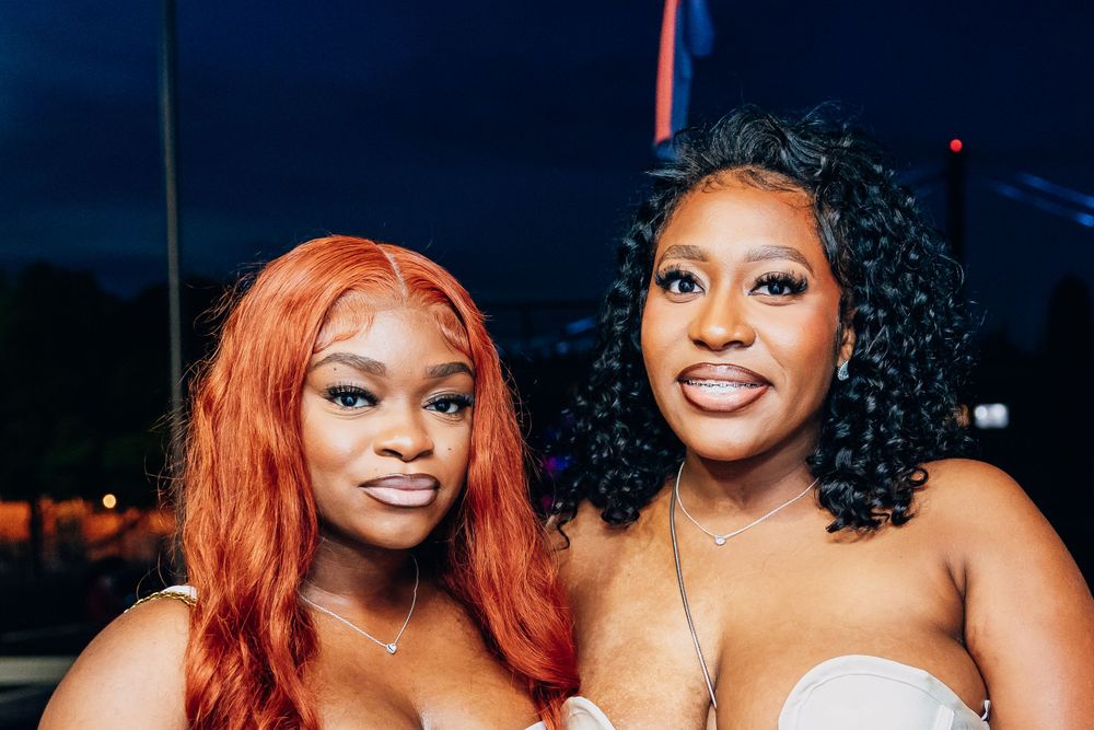 Two friends in white dresses smiling during nighttime boat celebration.