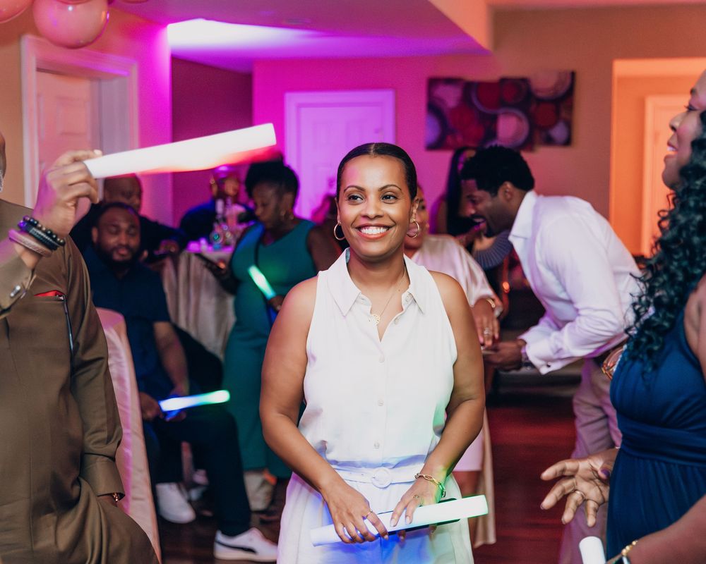 Woman smiling at indoor party with colorful glow sticks and pink lighting.