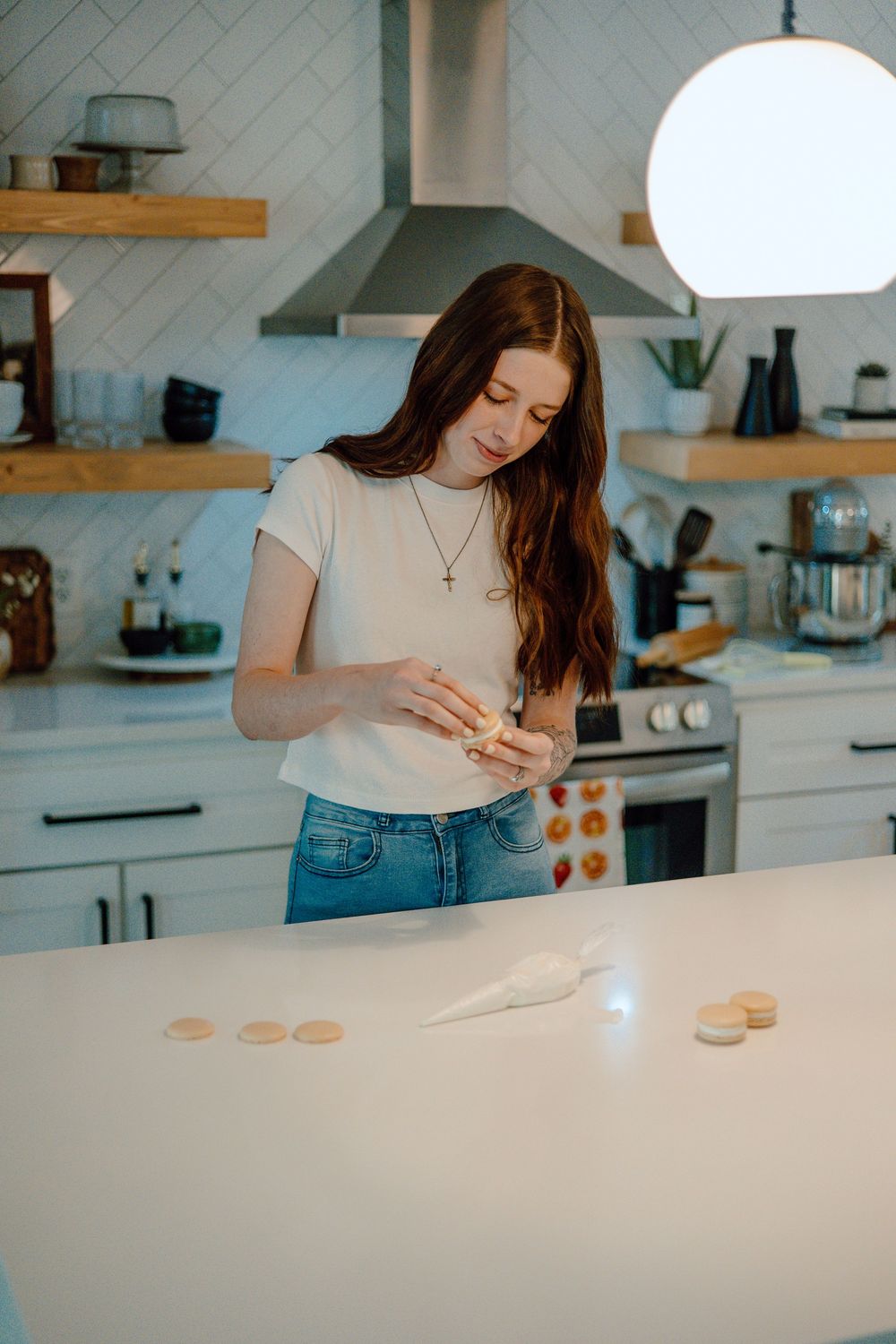 Someone decorating macarons on a white kitchen counter with natural lighting.