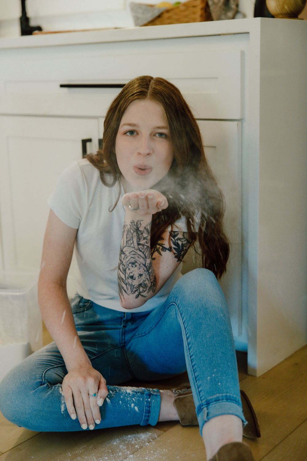 Person sitting on kitchen floor playing with flour and creating a mess.