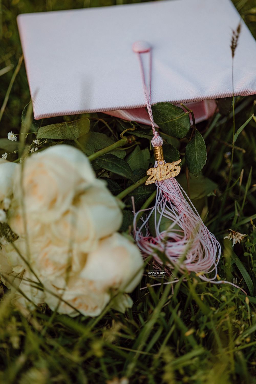 Graduation tassel and white roses arranged on grass with natural lighting.