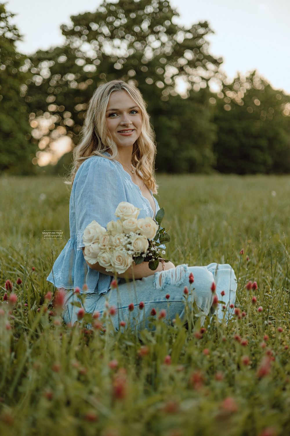 Outdoor portrait session in a meadow with white roses and red wildflowers.