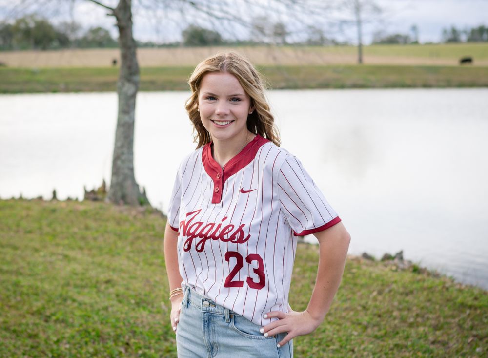 A Tate high school senior girl wears her softball jersey in a field with a pond in Cantonment, Florida