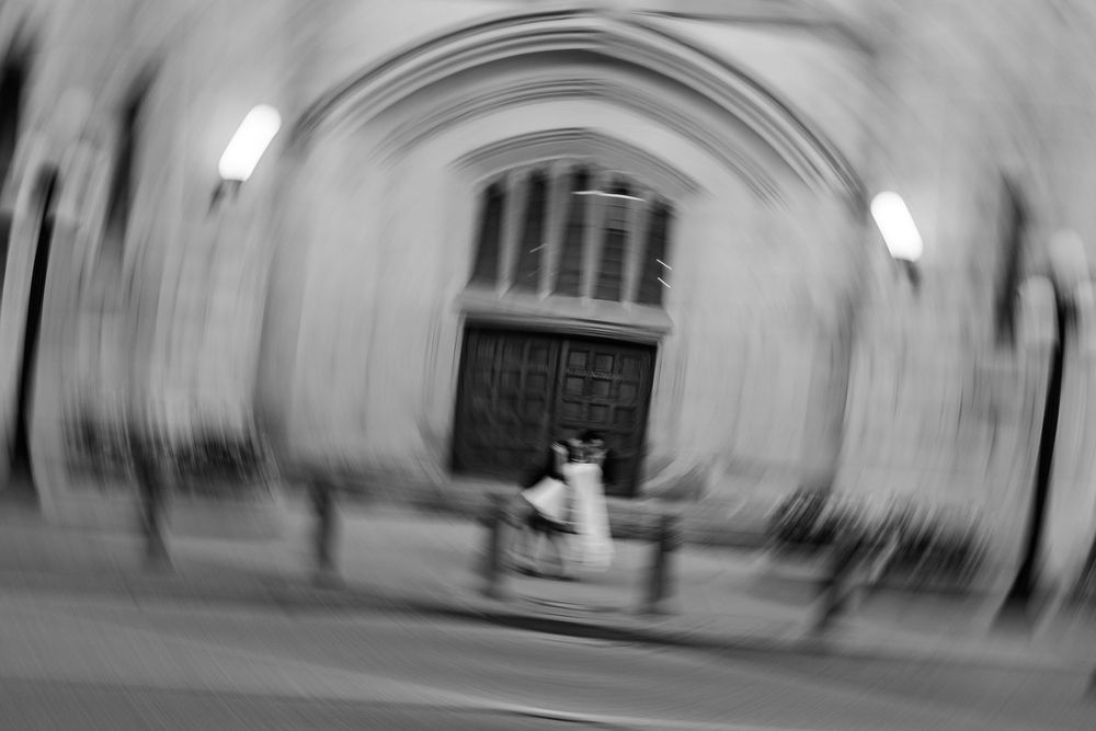 Blurry black and white photo of a couple standing before a grand church entrance with arched doorway.