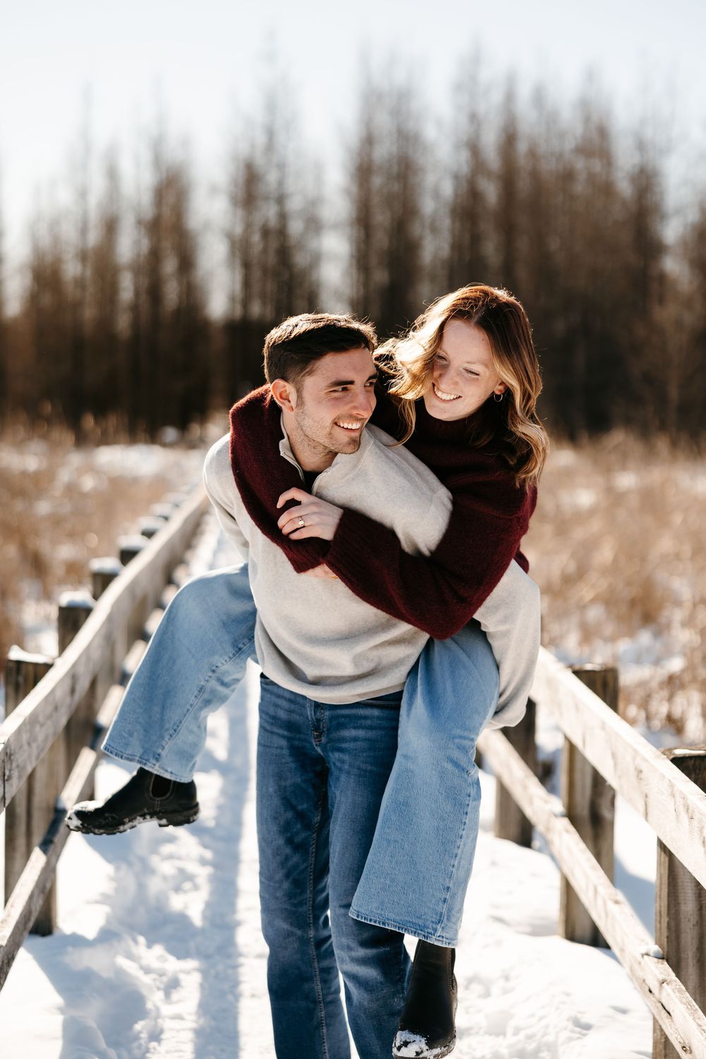 A couple shares a joyful moment on a snowy wooden boardwalk surrounded by winter scenery.