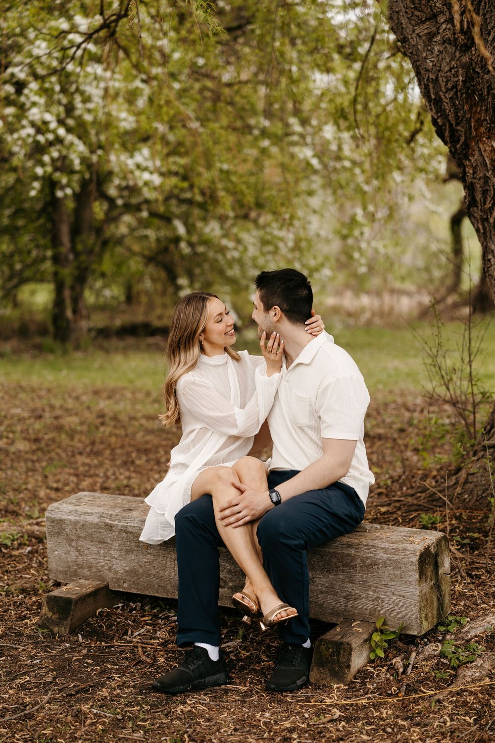 Couple sitting on a rustic wooden bench in a blooming garden, sharing a tender romantic moment outdoors.