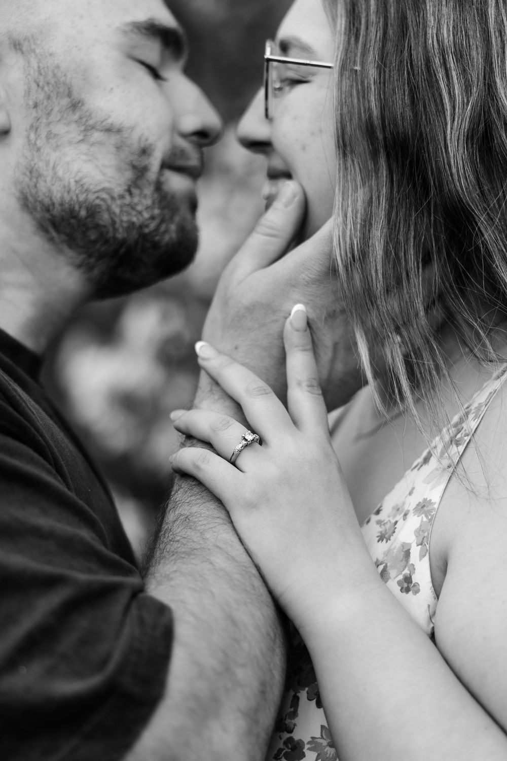Black and white photo of a couple about to kiss, woman wearing an engagement ring touching man's face.