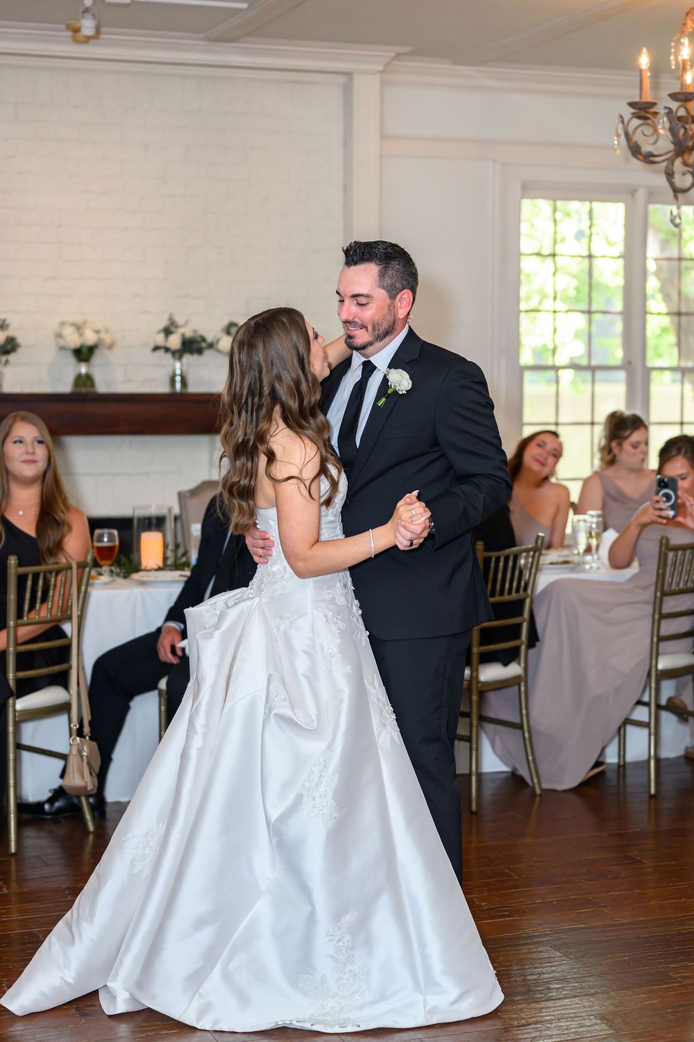 Bride and groom share their first dance at elegant wedding reception with guests seated at gold chairs.