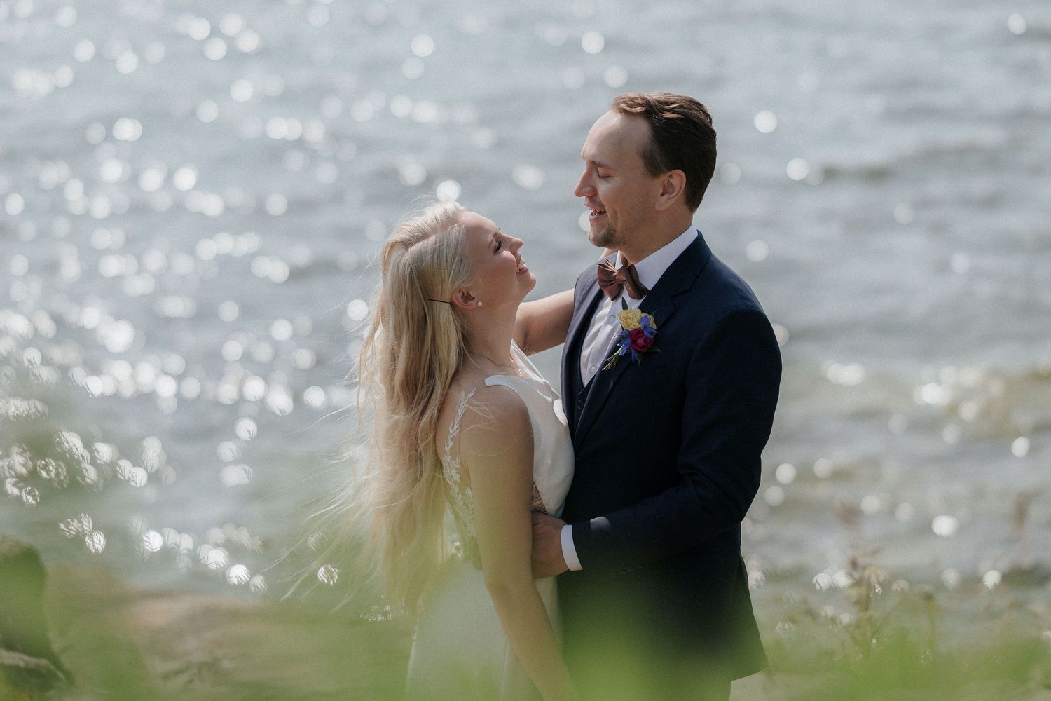 Wedding couple embracing in garden setting with lake view and colorful bouquet.