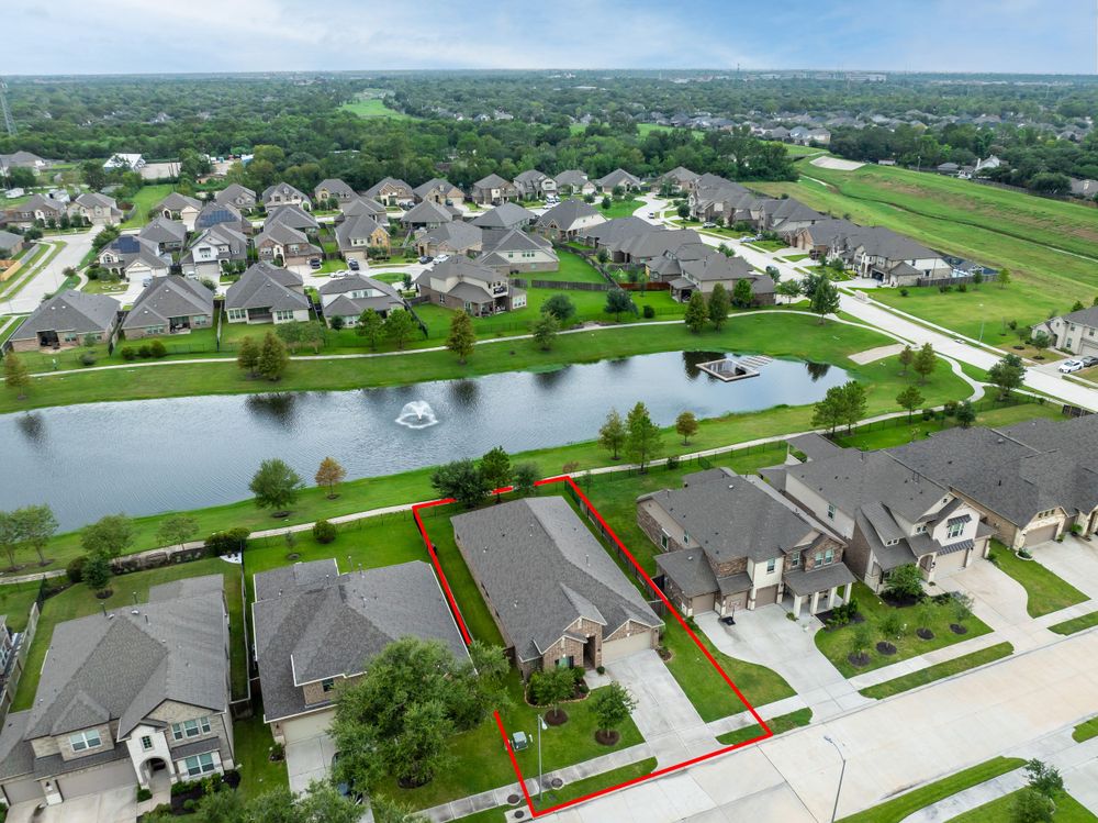 Drone shot of residential community with houses surrounding a peaceful pond and landscaped grounds.
