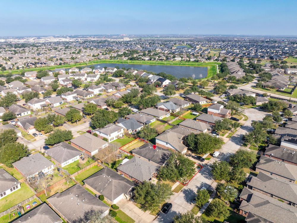Aerial view of suburban neighborhood with houses surrounding a large lake under blue sky in residential area.