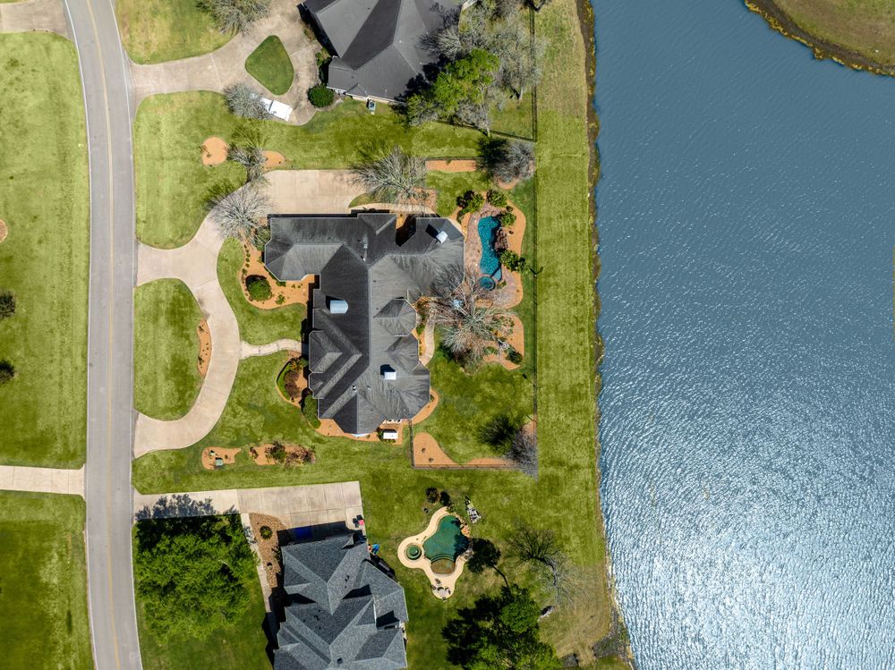 Aerial drone view of luxury waterfront homes with pools and landscaped yards along a curved residential street.