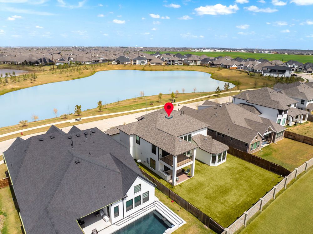 Aerial view of modern suburban homes with backyard pools along a scenic lakefront community under blue skies.