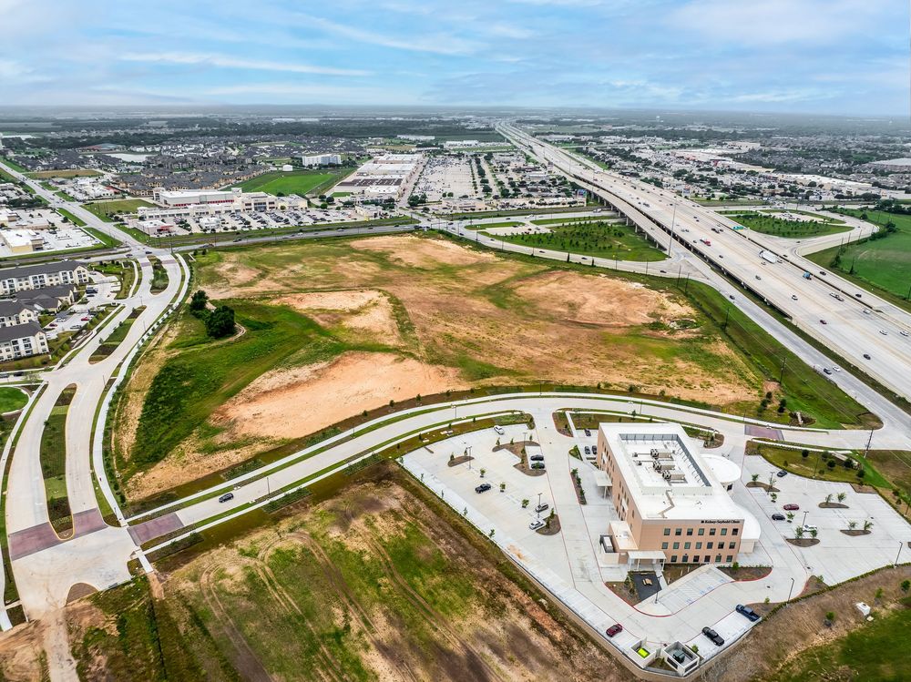 Aerial view of undeveloped land between highways and commercial development in an urban area.