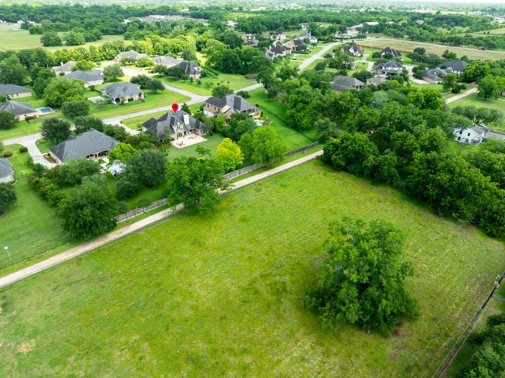 Aerial view of rural neighborhood properties with green lawns, houses, and mature trees in a residential subdivision.
