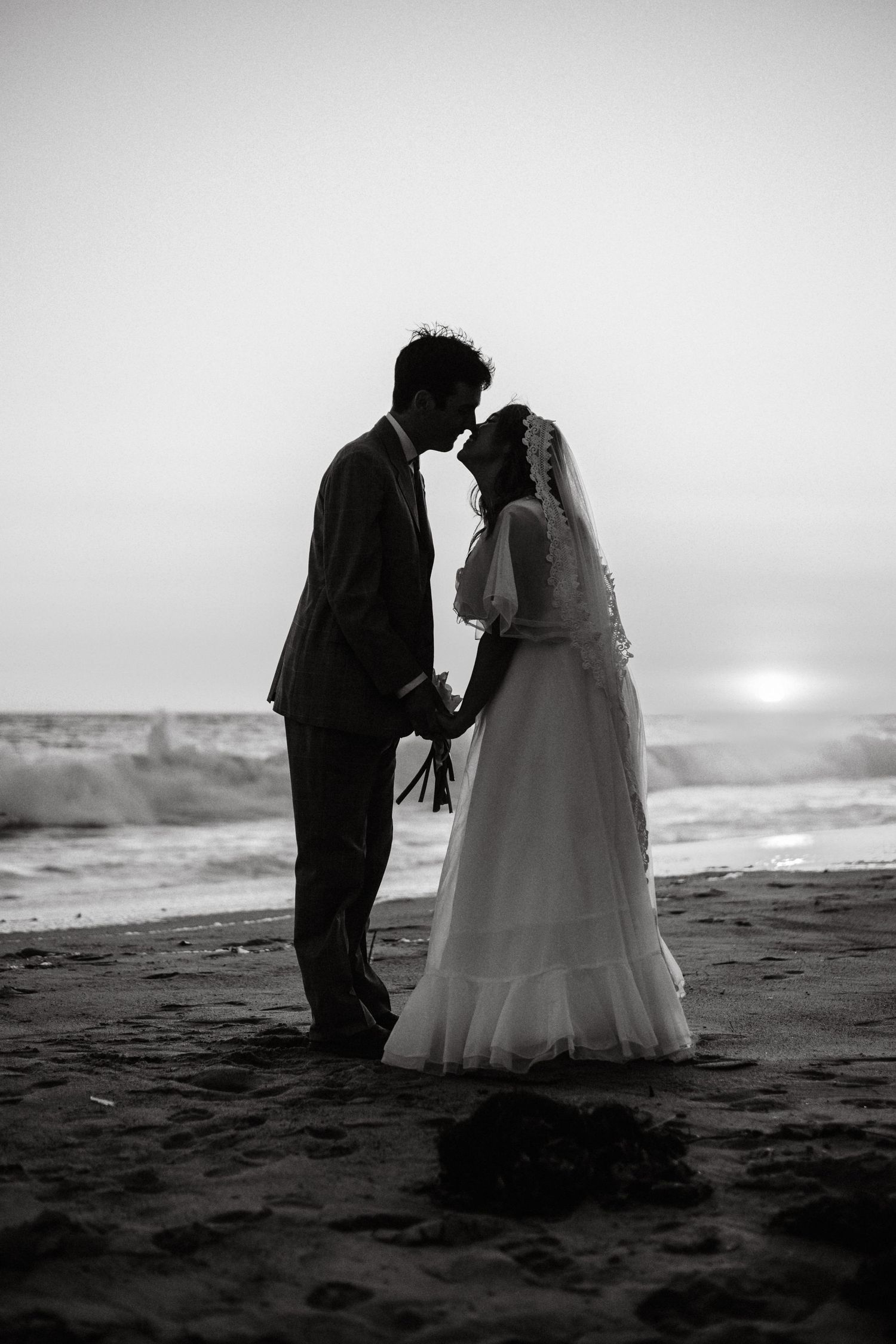A romantic black and white photo series of newlyweds sharing intimate moments on a misty beach at sunset.