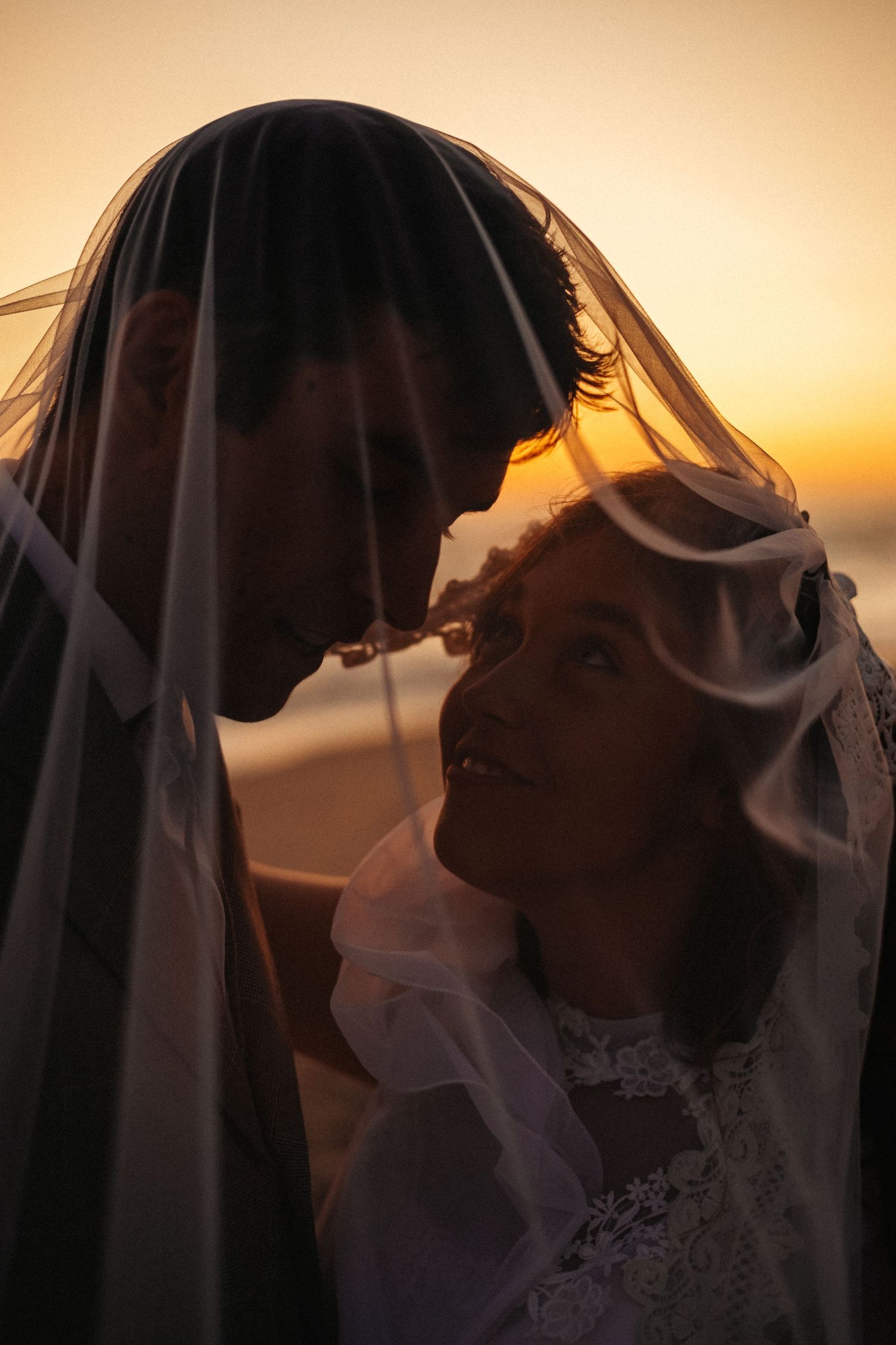 Silhouetted couple in wedding attire share an intimate moment against a golden sunset backdrop.