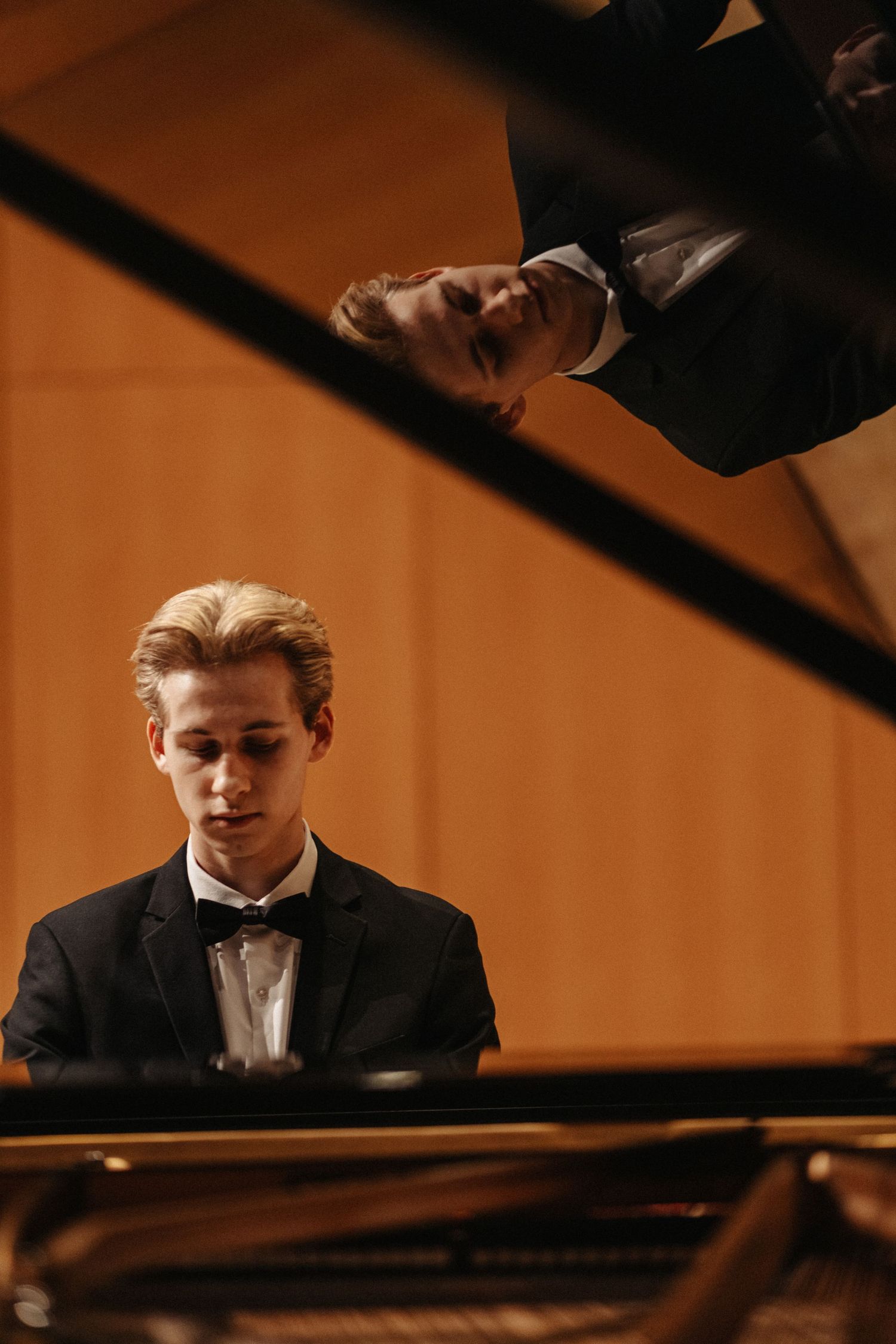 Classical pianist performing at a grand piano in formal attire under warm stage lighting.