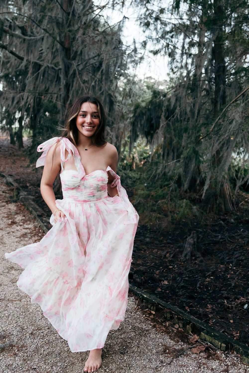 Ethereal portrait in flowing pink floral dress on mossy forest path.