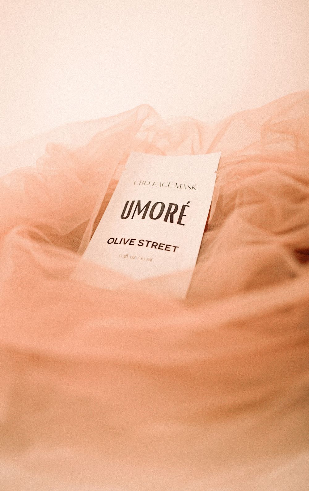 Umore Olive Street product packaging photographed with dreamy pink tones and soft fabric.