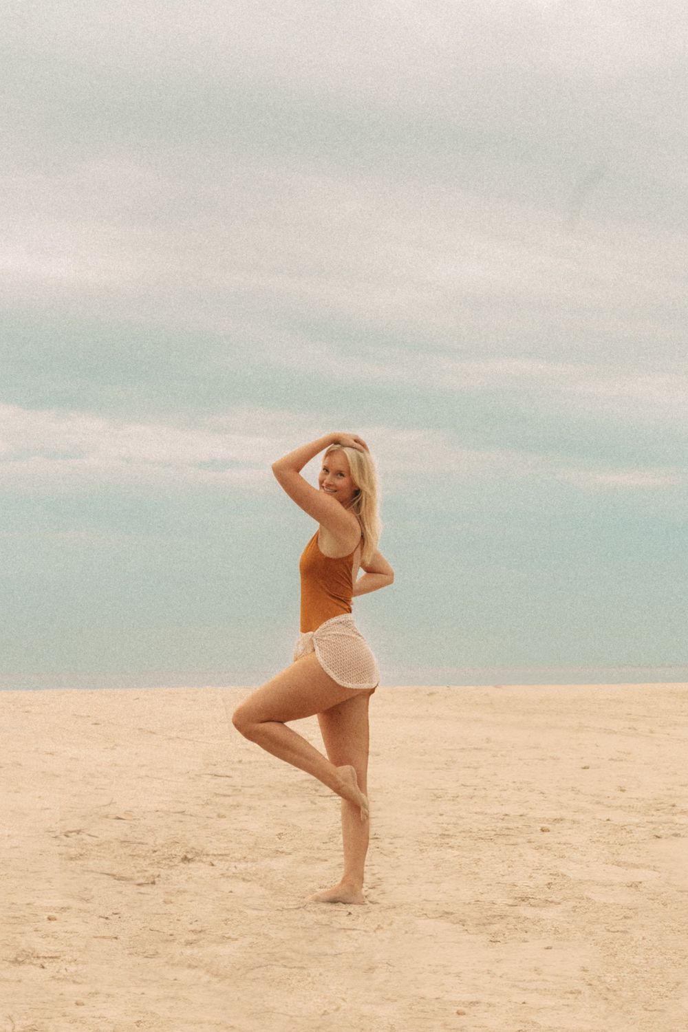 A silhouette of a dancer performing a graceful pose on a sandy beach under a soft pastel sky.