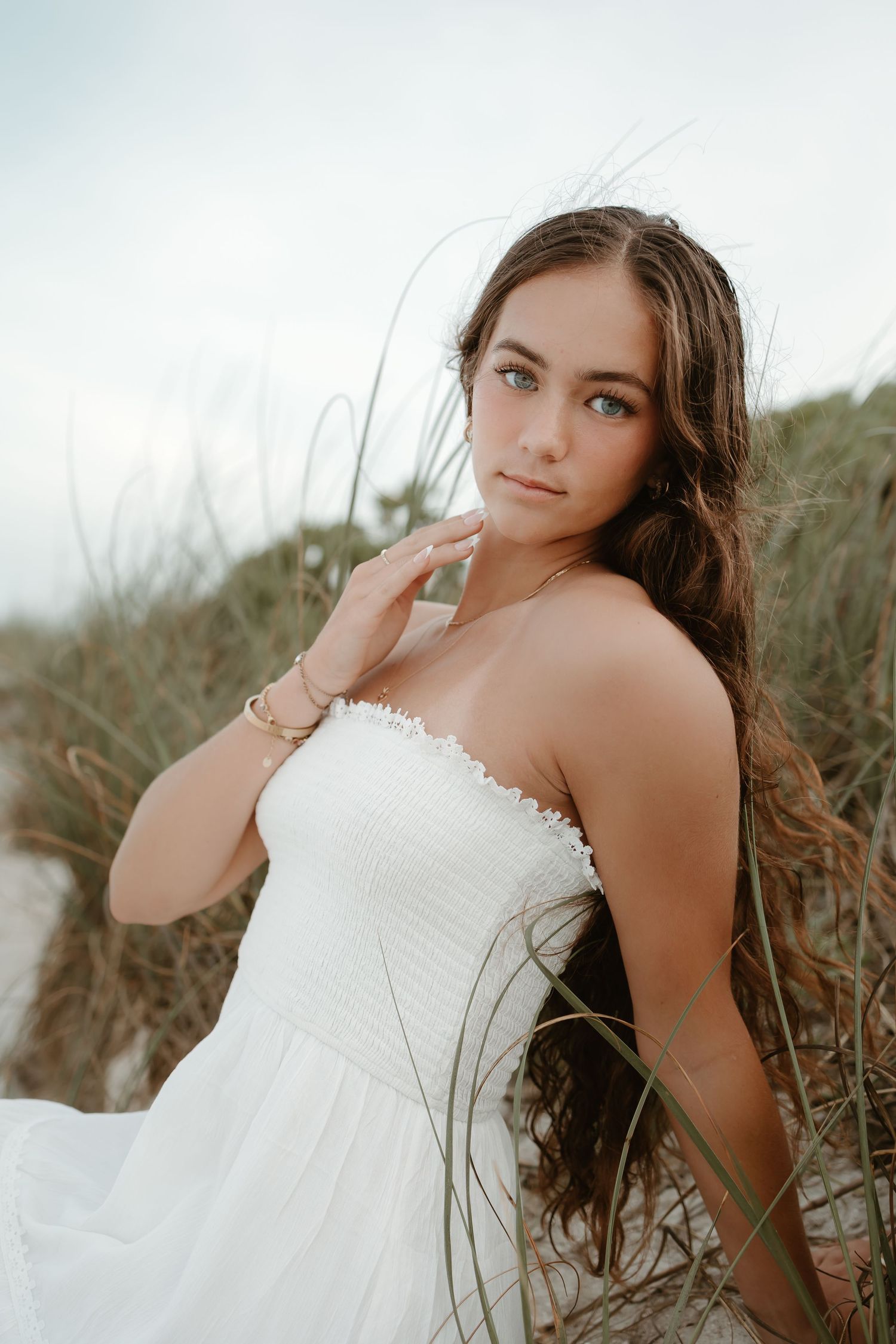 Woman in white dress poses gracefully in natural outdoor setting with soft lighting.