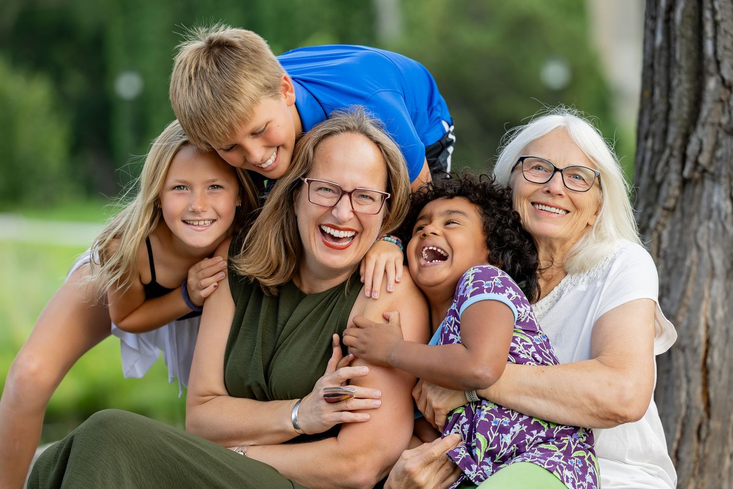 Family members share joyful moments together while posing outdoors near trees.