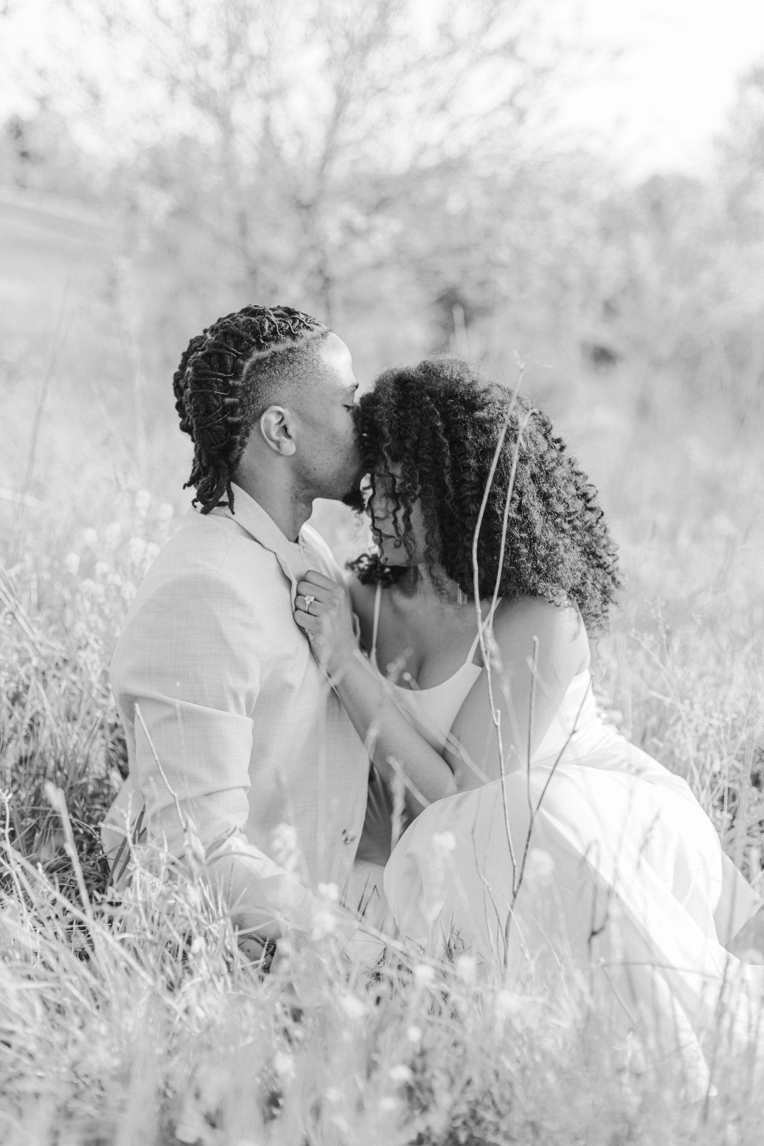 A romantic black and white portrait of a couple sharing an intimate moment in a sunlit field.