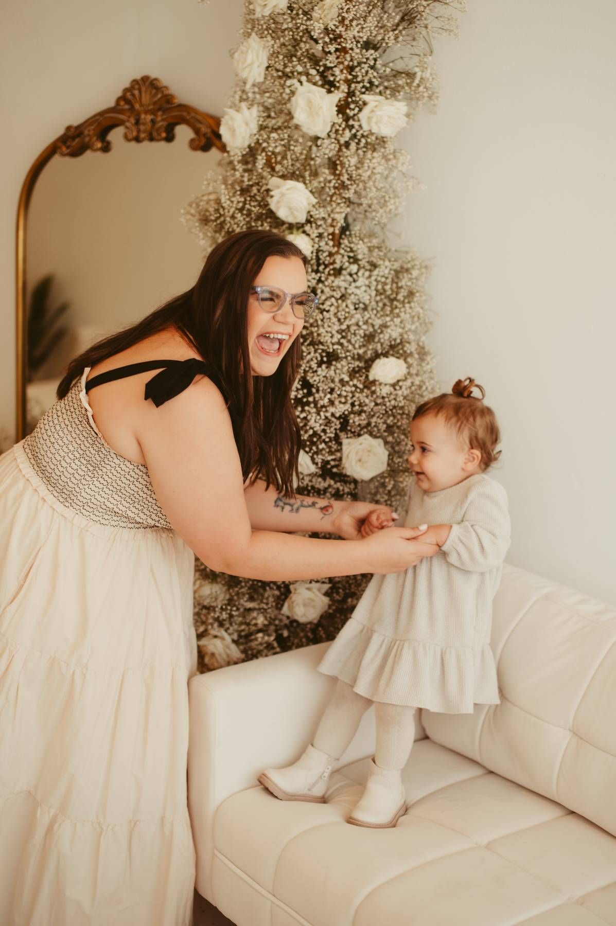 Mother and child play together on white couch with floral holiday decorations.