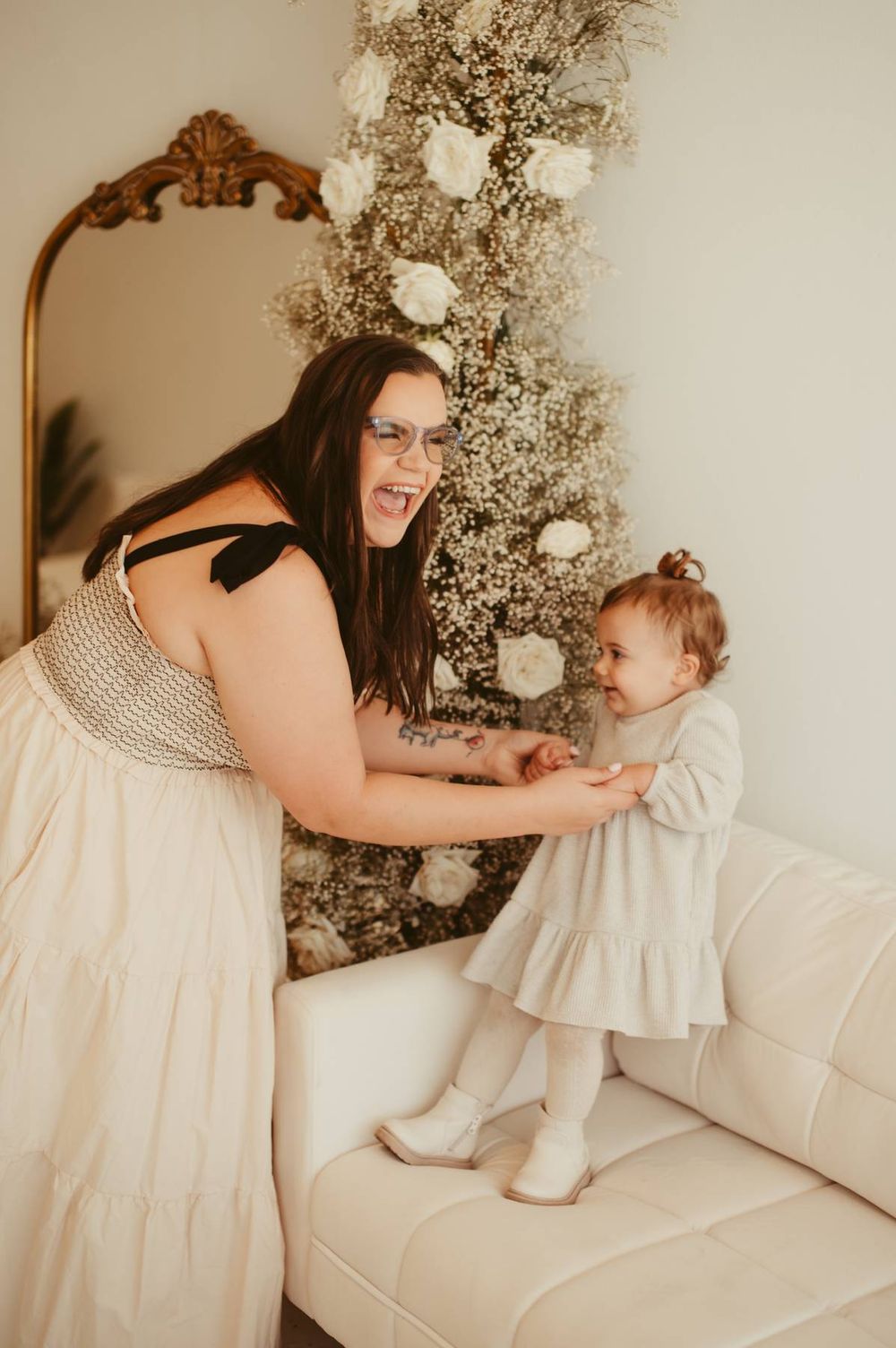 Mother and child play together on white couch with floral holiday decorations.