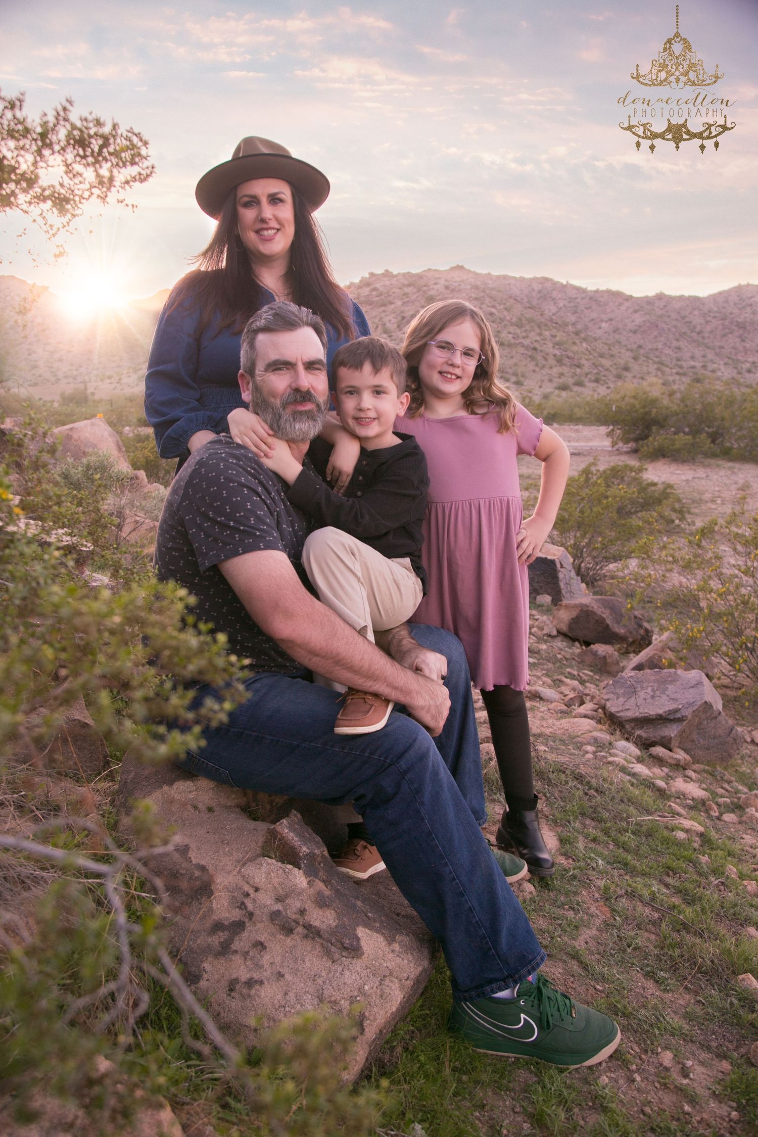 Family of four posing on desert rocks at golden sunset with mountains in the background.