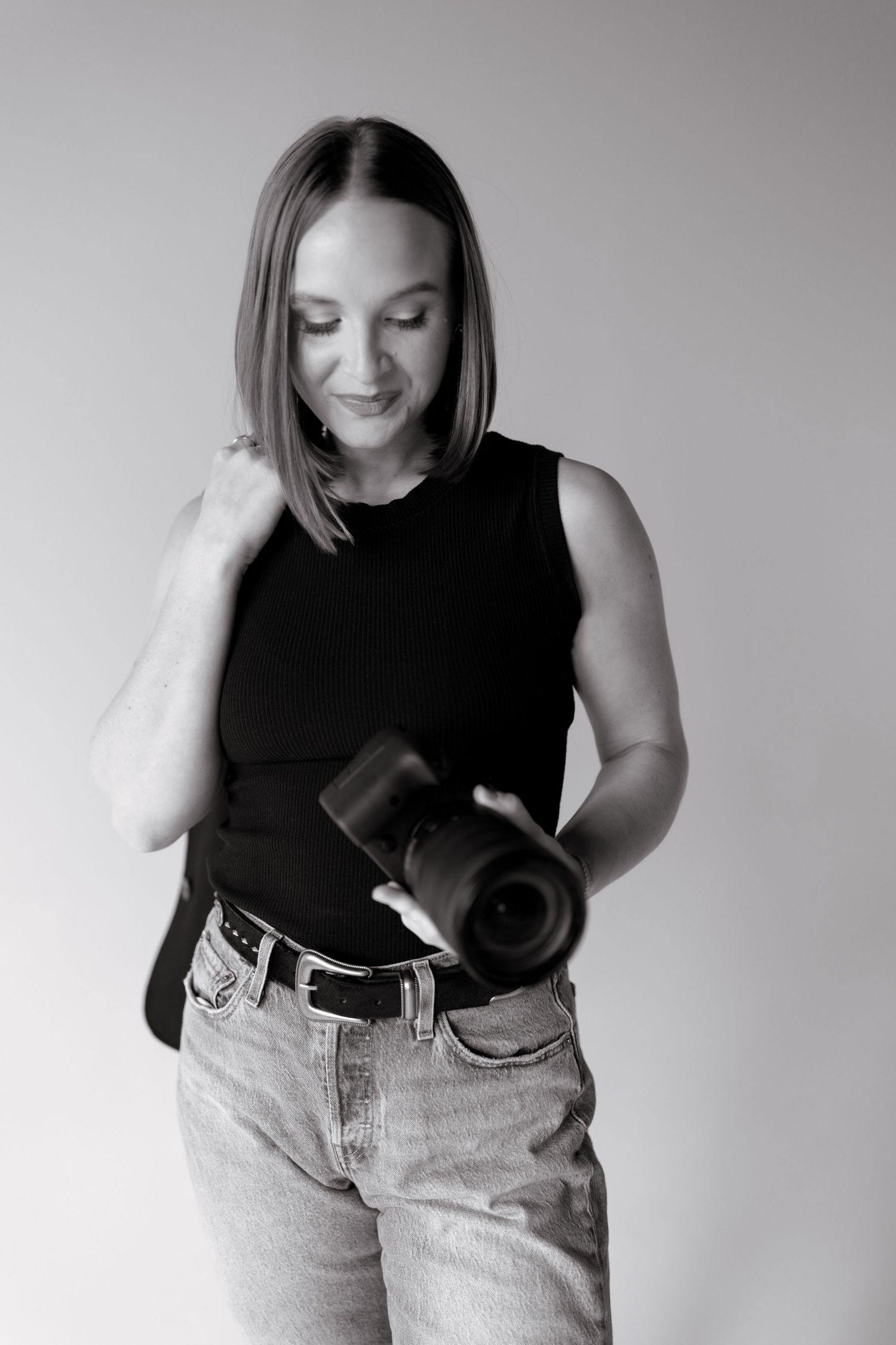 Black and white portrait of someone sitting casually in jeans against studio backdrop.