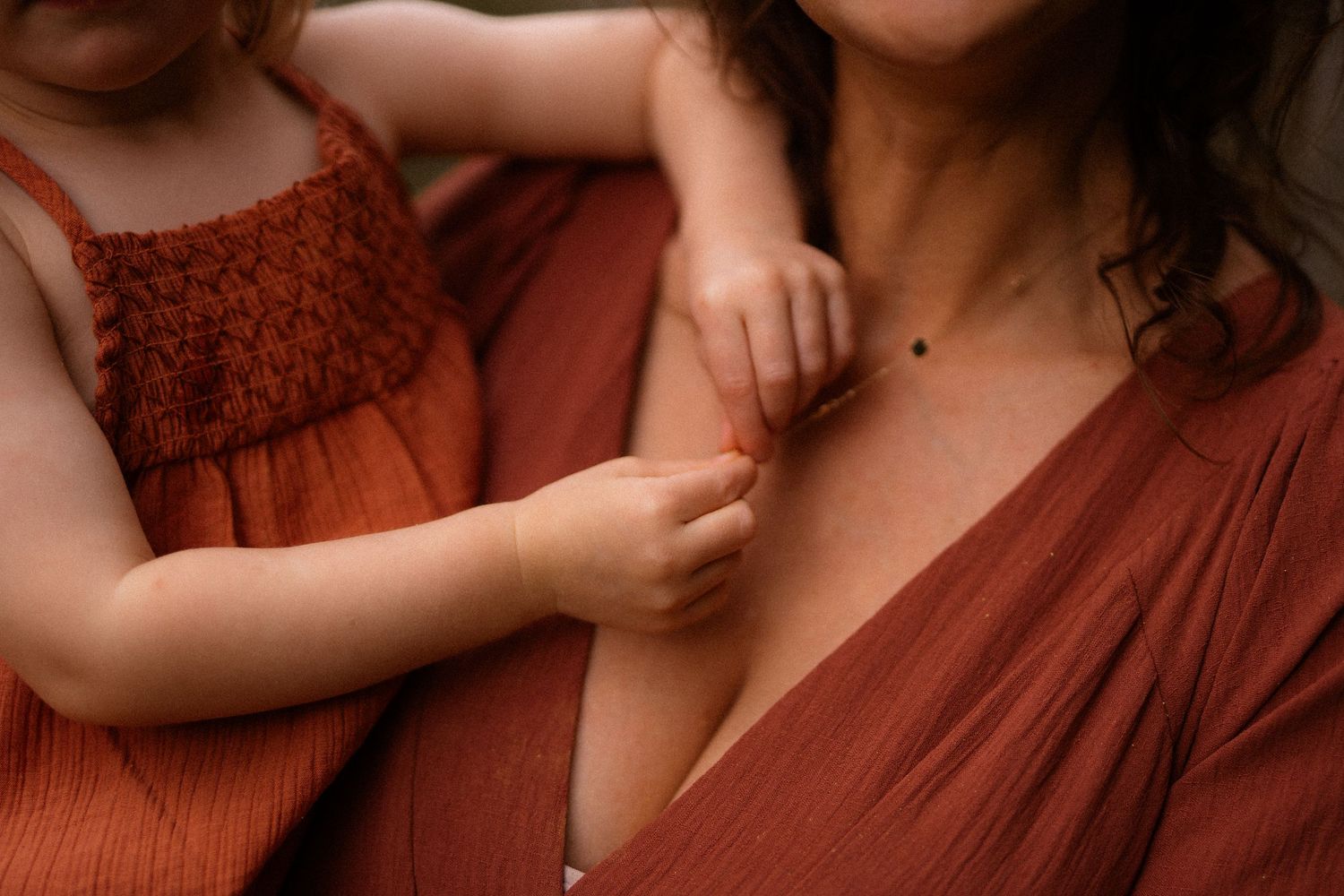 Close up of a tender moment in warm tones with gentle touching between a parent and child wearing rust-colored clothing.