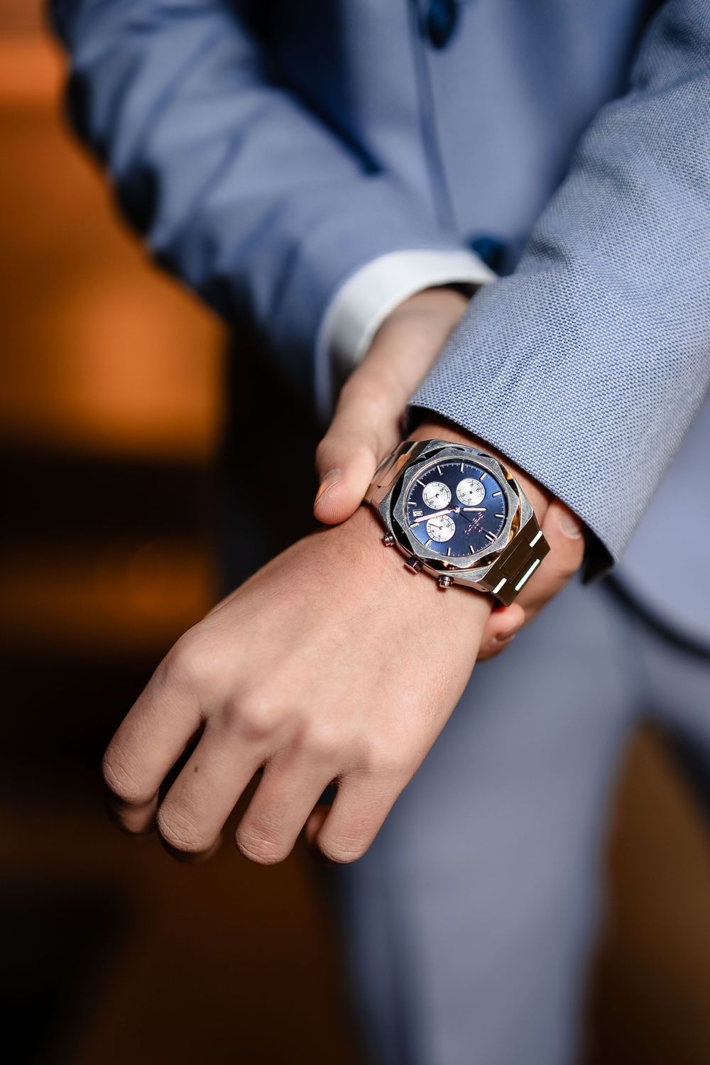 Close-up detail shots of luxury watch with blue face against light blue suit sleeve.