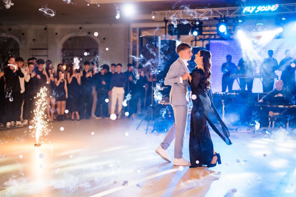 A lively dance floor scene with blue lighting and sparkler effects at an event.