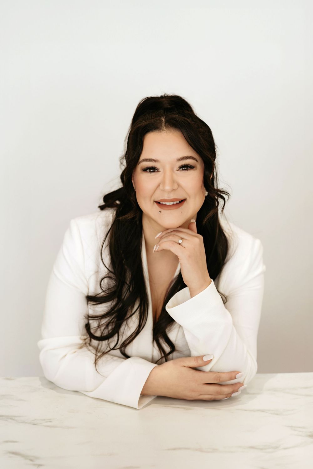 Professional headshot of a woman in a white blazer smiling warmly against a light background.