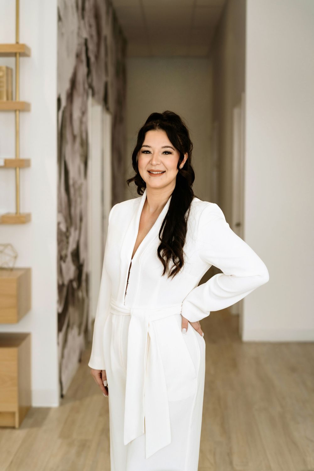 Cheerful portrait of person in white wrap dress standing in modern interior hallway.
