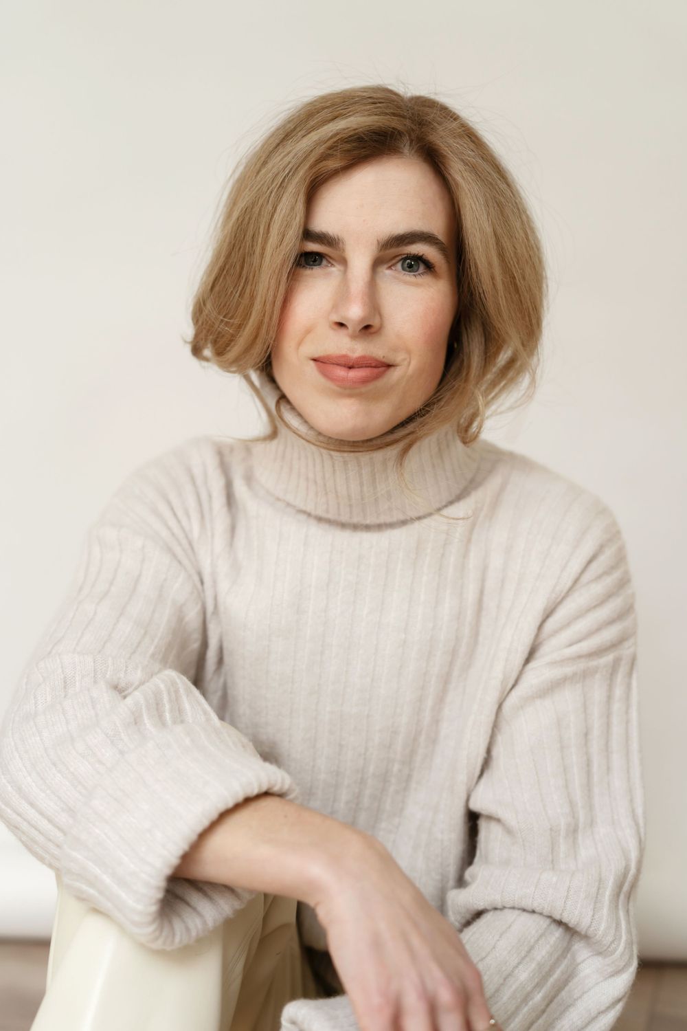 Professional portrait of a woman in beige turtleneck sweater with voluminous blonde hair.