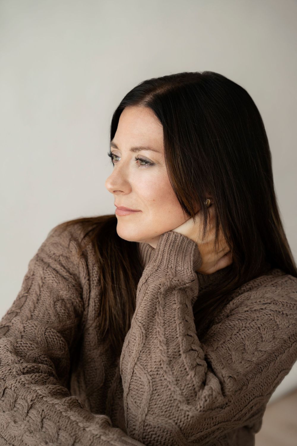 Professional portrait of a person in a brown cable knit sweater looking pensively to the side.