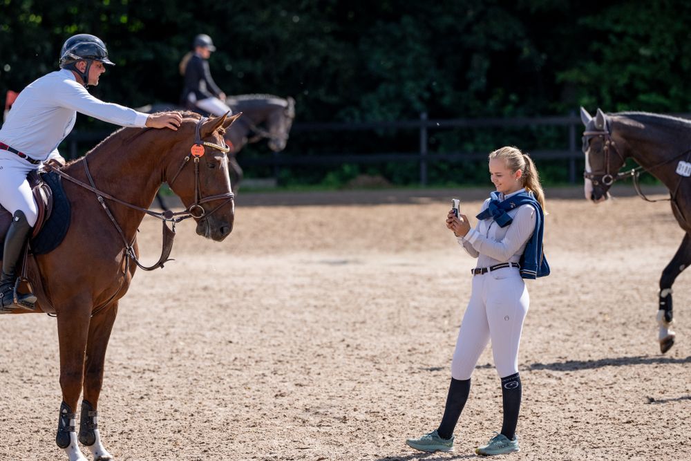 Equestrians interacting during training session in sandy outdoor arena.