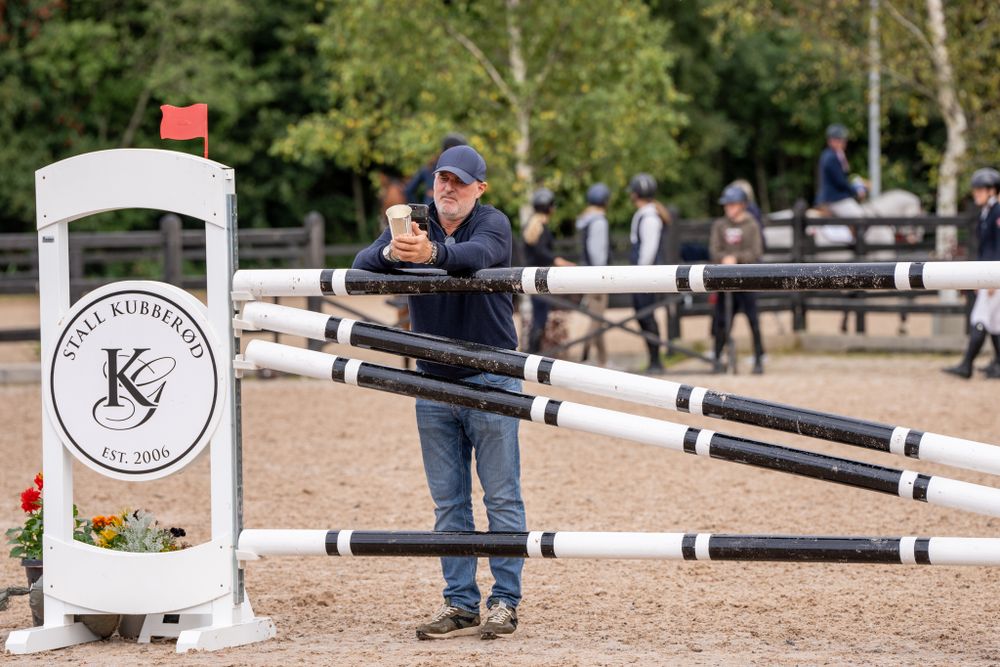 Person setting up equestrian jump equipment in a sandy arena with branded jumps.