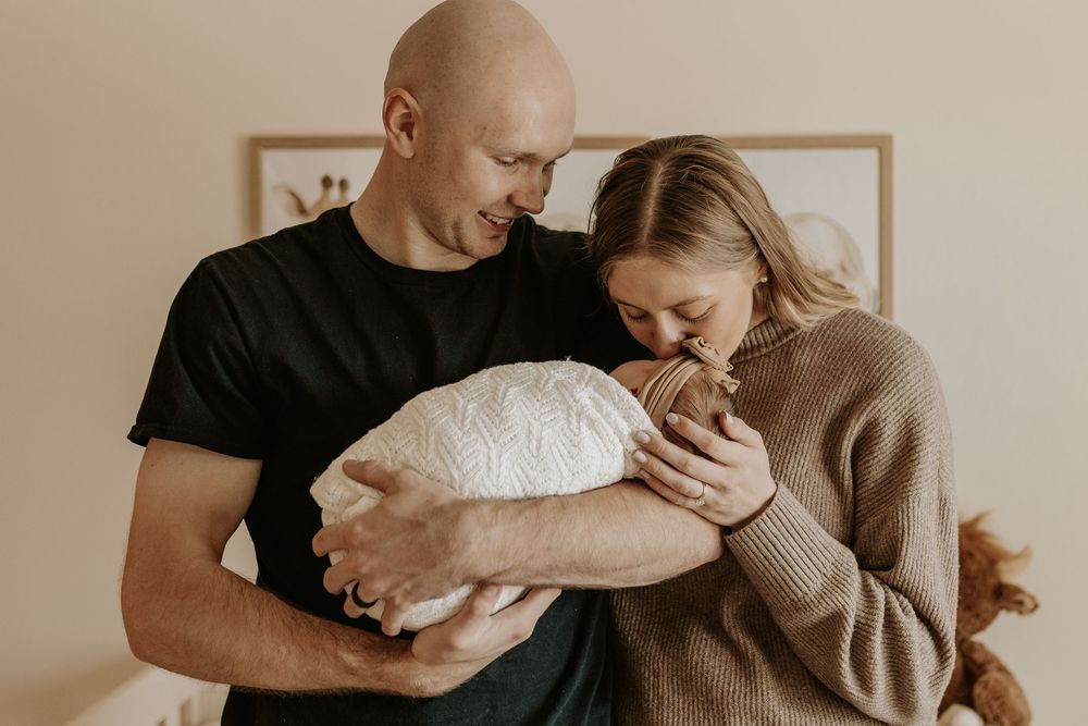 New parents tenderly cradling their sleeping newborn baby, sharing a loving family moment together.