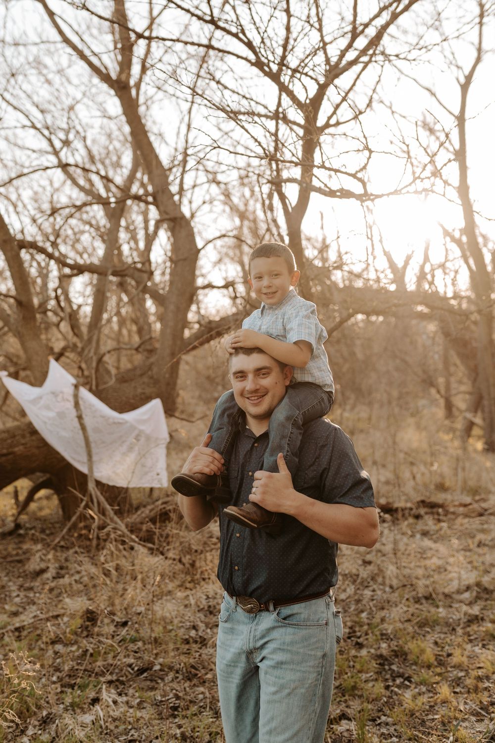 Smiling father carries young son on shoulders in a sunlit autumn forest setting.