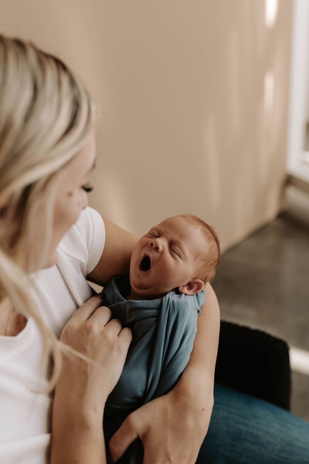 Newborn baby wrapped in teal fabric yawning during intimate moment.