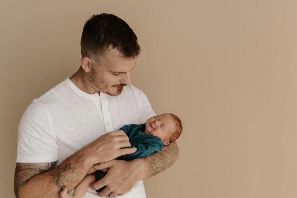 Gentle parent-child moment with sleeping newborn wrapped in teal fabric.