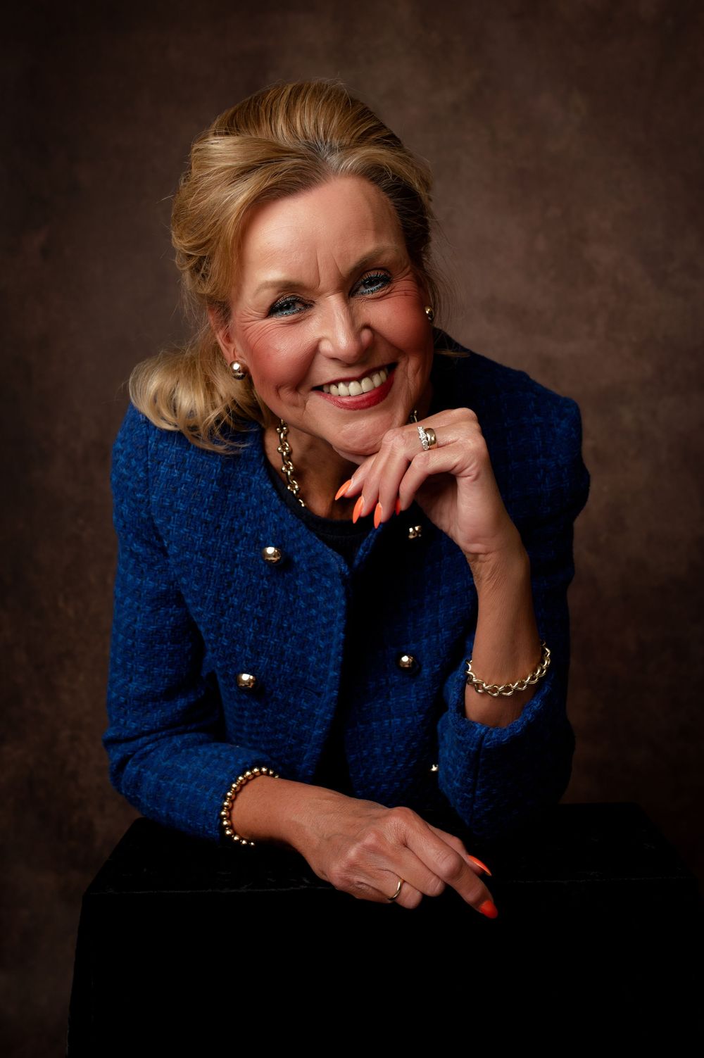 Professional headshot series of woman in navy blazer with gold buttons showing various warm expressions against dark background.
