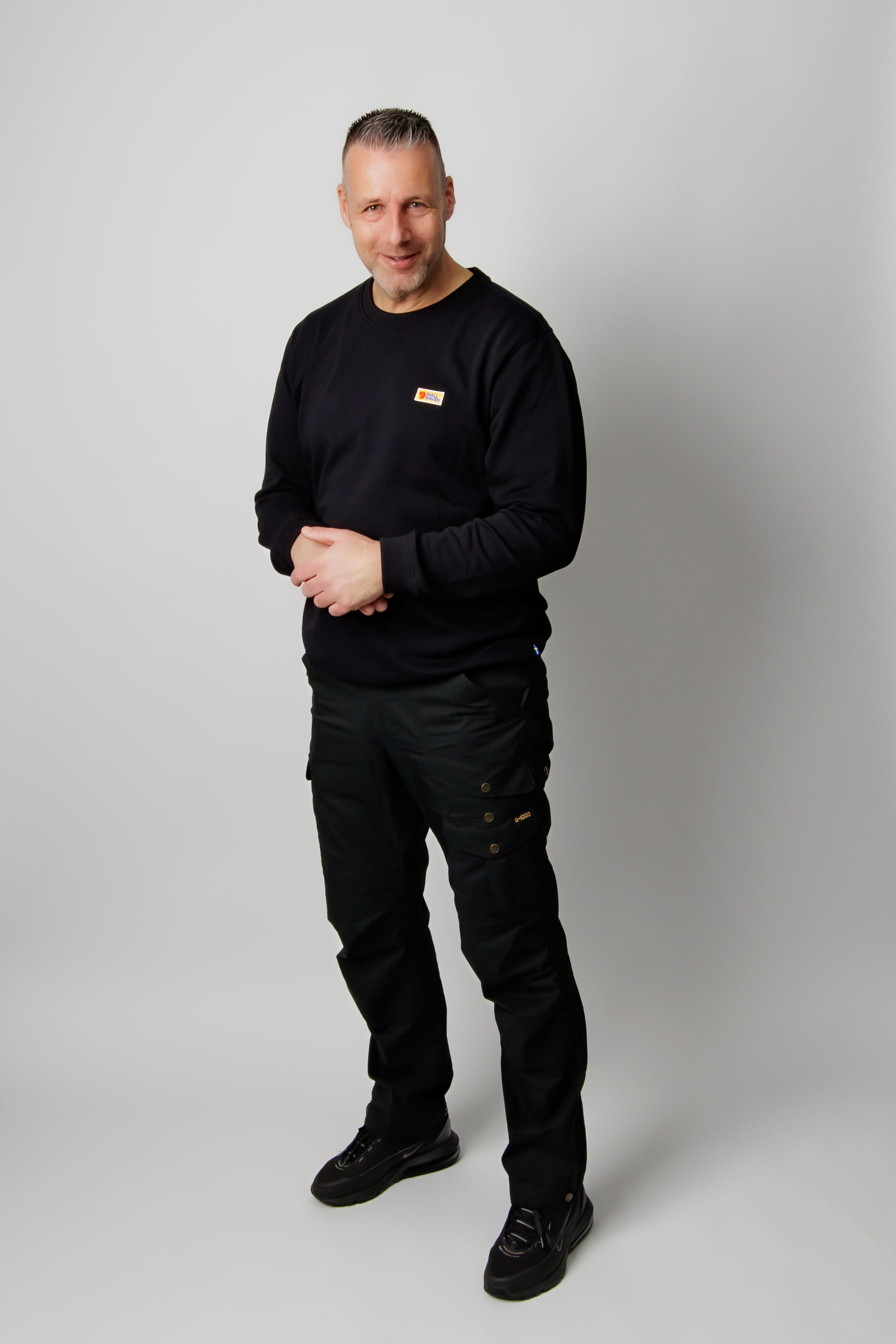 Three studio shots of a person in all-black attire posing against a light gray background.